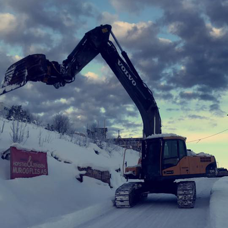 Gravemaskin som graver på en isete og snødekt vei